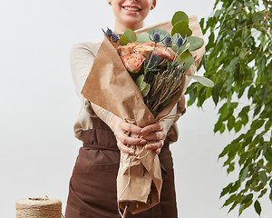 Image showing Smiling girl florist with beautiful bouquet in her hands on a light background with green leaves. Mother\'s Day holiday.