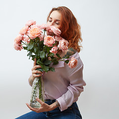 Image showing Sexy girl with a bouquet of delicate pink roses in a transparent vase on a gray background with copy space. St. Valentine\'s Day