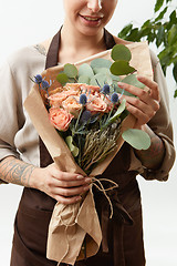 Image showing Smilling girl florist with creative bouquet from fresh flowers roses in a paper on a light background. Close-up. Congratulation card.