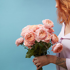 Image showing Gentle pink roses in the hands of a girl with a tattoo on a blue background with copy space for text. Birthday present