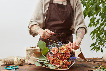 Image showing Florist workplace - woman\'s hands are arranging a new bouquet with roses and decorative green leaves on a wooden table, process step by step. Place for text. Mother\'s Day.