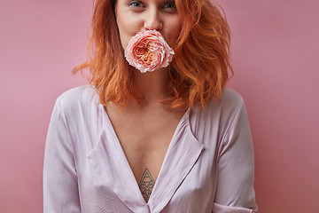 Image showing Pretty woman holding a rose bud in her mouth around a pink backg