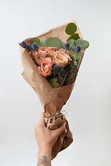 Image showing Female hand gives bunch with coral roses and green leaf on light background, copy space. Gift for Mother or Woman\'s Day.