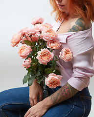 Image showing A bouquet of pink roses in a vase holds a girl with a tattoo on a gray background with copy space. St. Valentine\'s Day