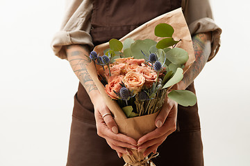 Image showing Close-up of greeting bouquet from fresh roses, eryngium and green leaves a in a female\'s hands with tattoo on a gray background. Place for text. Gift for Mother\'s Day.