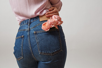 Image showing Attractive woman\'s butt in a blue jeans and fresh roses living coral color in a back pocket on a light gray background, place for text. Congratulation card.