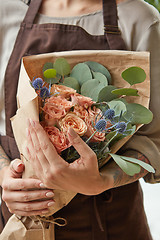 Image showing Florist in a brown apron with a bouquet of coral roses. Girl is holding a flowers in her hands. Close-up view. The gift to Mother\'s Day.