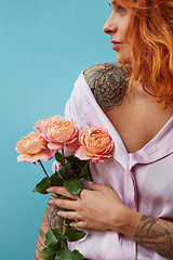 Image showing Attractive female with tattoo on her shoulders and hands holds bouquet of coral roses on a blue background, place for text. A gift for Mother\'s Day.