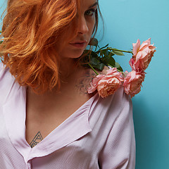 Image showing Young cute girl with a bouquet of living coral roses on her shoulders with tattoo on a blue background. Postcard on Mother\'s day