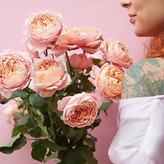 Image showing A young girl with a tattoo is holding a bouquet of elegant pink roses around her pink background.