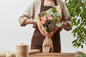 Image showing Girl\'s florist hands hold fresh natural bouquet from fragrant flowers living coral color roses, green leaf in a paper on a background of gray wall, copy space.