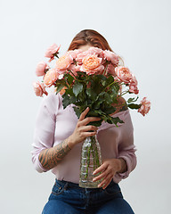 Image showing A woman with a tattoo holding a large bouquet of pink roses in a glass vase around a gray background with copy space. Mother\'s Day Gift