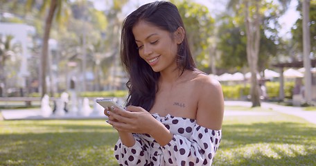 Image showing Pleasant Asian woman with open shoulder texting in smartphone with smile