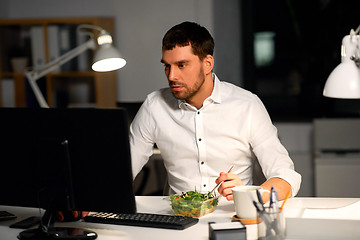 Image showing businessman at computer eating at night office