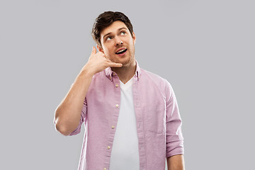 Image showing young man showing phone call gesture over grey