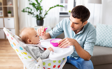 Image showing father feeding happy baby in highchair at home