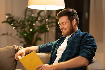 Image showing happy young man reading book at home in evening