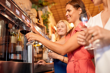 Image showing happy women pouring wine from dispenser at bar