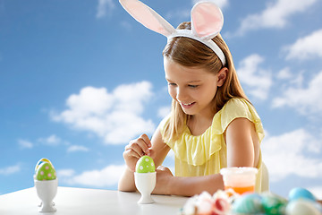 Image showing happy girl coloring easter egg over blue sky