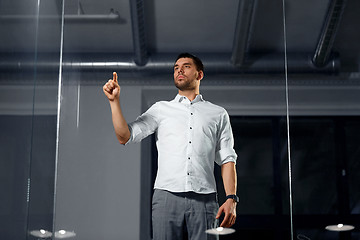 Image showing businessman touching glass wall at night office