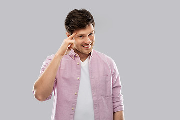 Image showing smiling young man pointing finger to his head
