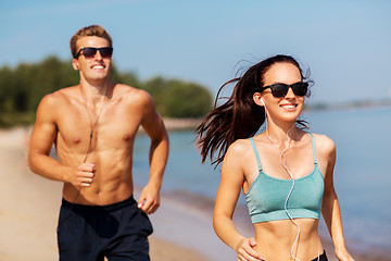 Image showing couple with earphones running along on beach