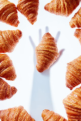 Image showing French croissants frame with hand shadow taking bakery on a light background.