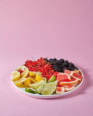 Image showing Set of different citrus fruits and berries in a plate presented on a pink background with copy space. Healthy Vitamin Food