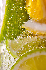 Image showing Macro photo of freshly made lemonade with pieces of lime, lemon and bubbles in a glass. Summer refreshing drink