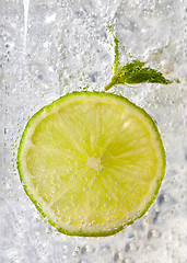 Image showing Macro photo of a piece of lime and mint leaf in a glass with ice and bubbles. Cold summer drink concept