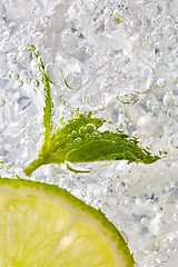 Image showing Fresh mint leaf and a slice of lime with bubbles in a glass with ice. Macro photo of refreshing drink