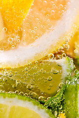 Image showing Pieces of citrus fruits of lemon and lime with bubbles in a glass of water. Macro photo of summer refreshing cocktail