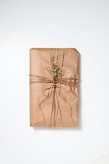 Image showing A gift wrapped in craft paper and decorated with flowers on a light background with copy space. Flat lay