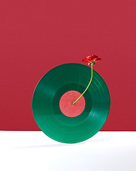 Image showing Composition of a red flower decorating a vinyl audio record on a double white red background with copy space