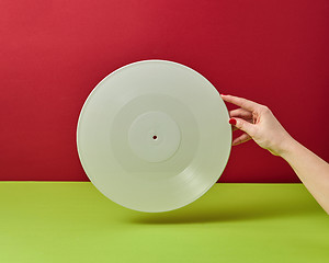 Image showing Woman\'s hand is holding a white vinyl audio record on a duotone red green background with a copy space.