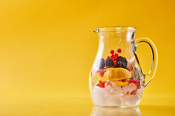 Image showing Glass jug with citrus, berries and ice on a yellow background.