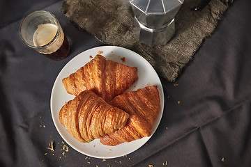 Image showing Coffee glass with freshly baked homemade croissants on a dark gray table