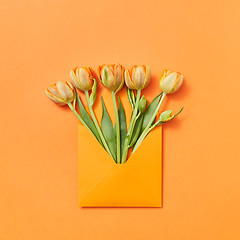 Image showing Fresh spring tulips as a gift in a craft envelope on an orange background.