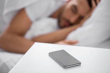 Image showing smartphone on bedside table near sleeping man