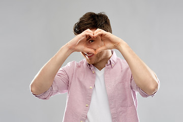 Image showing man making hand heart gesture over grey background