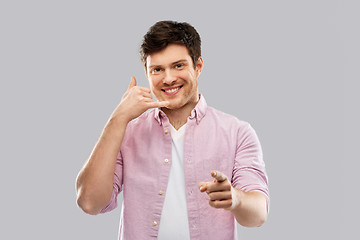 Image showing smiling young man showing phone call gesture