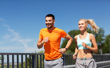 Image showing couple with fitness trackers running along bridge