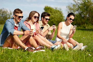 Image showing smiling friends with smartphones sitting on grass