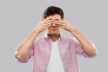 Image showing man closing his eyes by hands over grey background