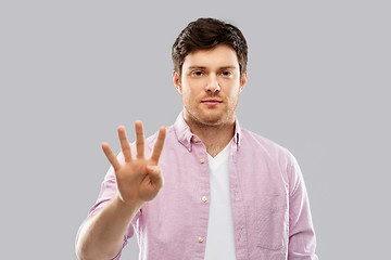 Image showing young man showing four fingers over grey