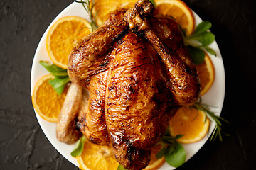 Image showing Roasted whole chicken or turkey served in white ceramic plate with oranges