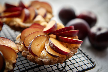 Image showing Homemade crumble tarts with fresh plum slices placed on iron baking grill