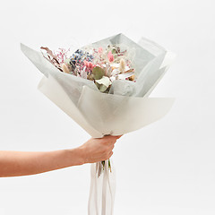 Image showing Greeting bouquet from flowers in a hand on a light backhround.