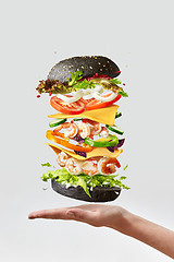 Image showing Healthy homemade burger with fresh shrimp and vegetables above the hand on a light background.