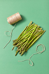Image showing Bunch of natural healthy asparagus and a coil of rope on a green background.